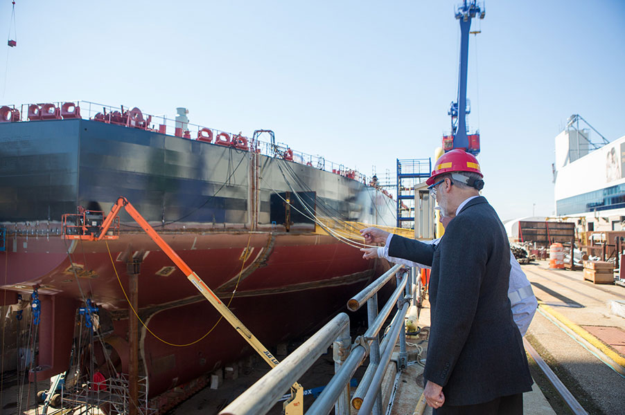 PA Governor Tom Wolf stands discussing the Philly Shipyard Apprentice Training Academy while examining a large ship in drydock.