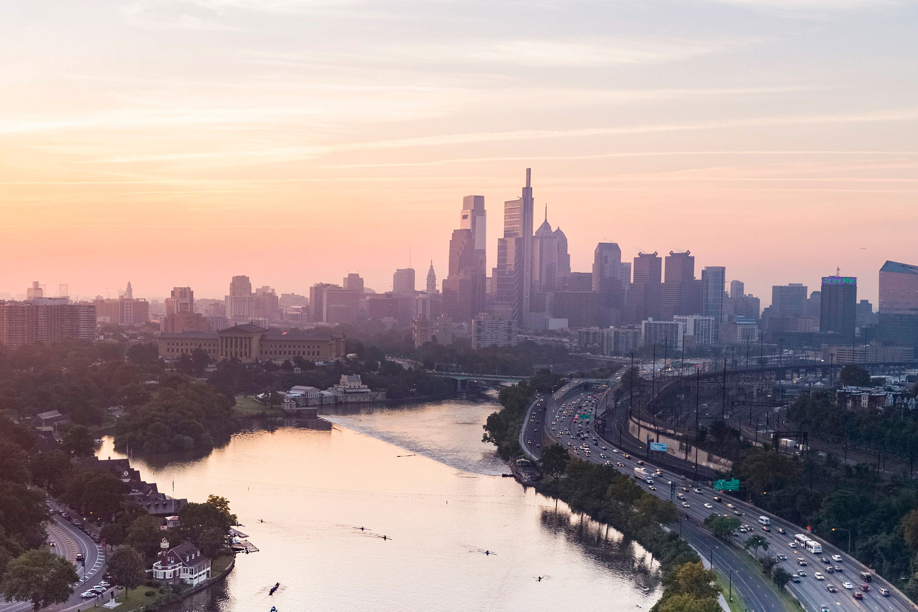 Philadelphia skyline with an orange and pink glow at sunset looking across the Delaware River.