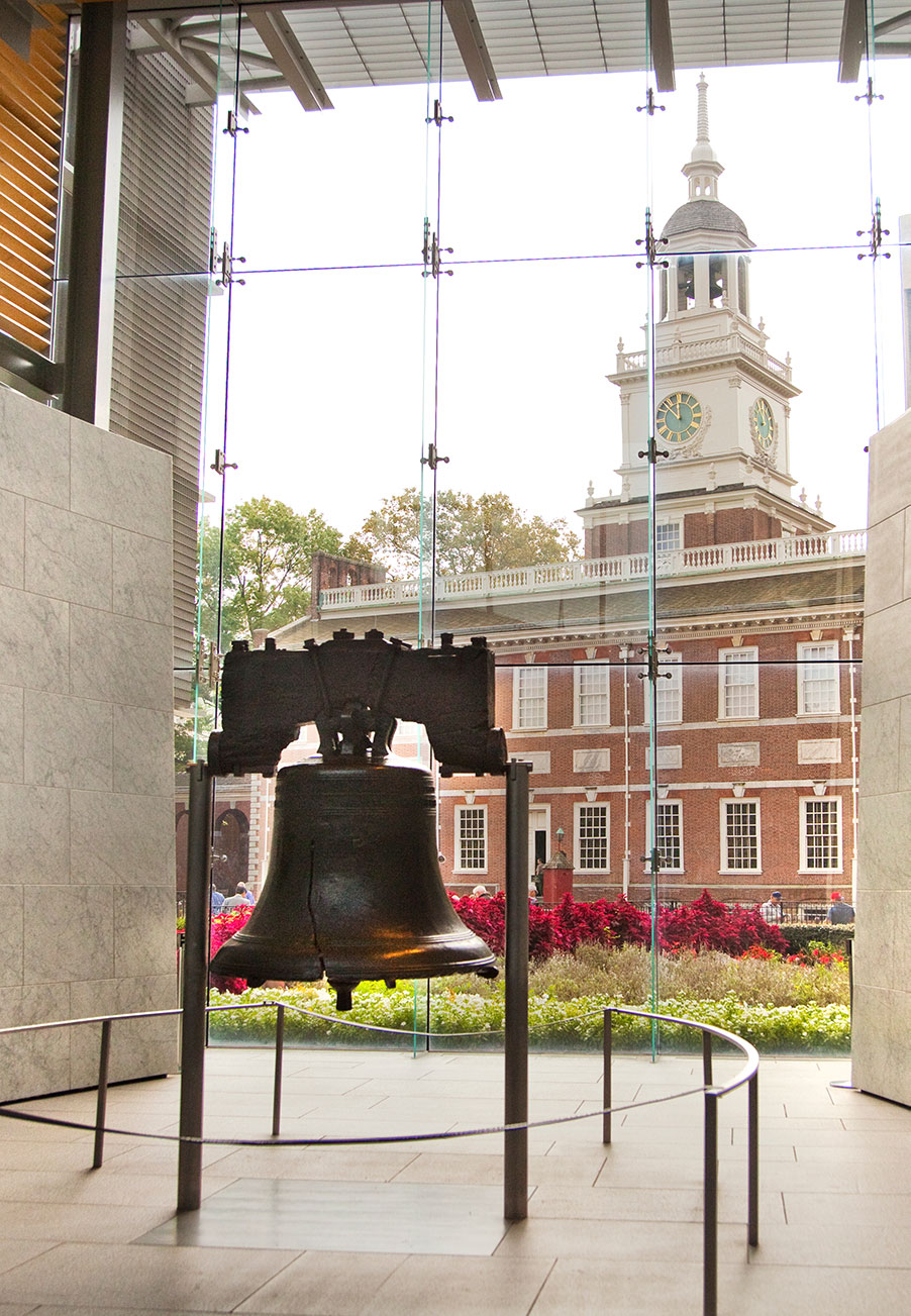 The Liberty Bell inside the visitors center with Independence Hall visible through the windows in the background.