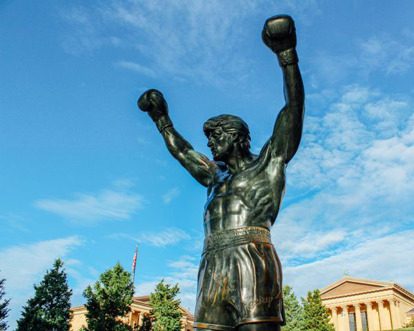 The bronze statue of Rocky Balboa from the Rocky movies with arms raised above his head and wearing boxing gloves.