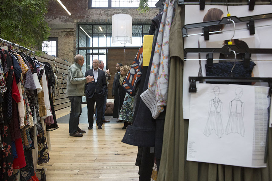 PA Governor Tom Wolf stands discussing employment opportunites with Urban Outfitters staff at the headquarters in the Philadelphia Navy Yard surrouned by racks of clothing and design sketches.